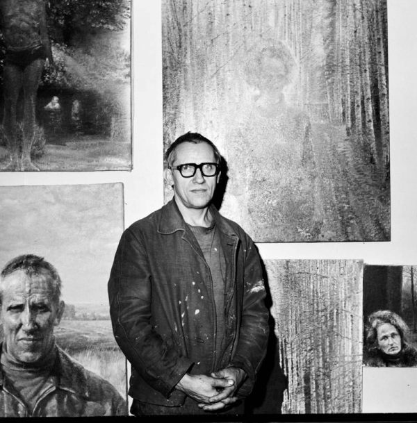 Artist Oleg Vassiliev standing with paintings