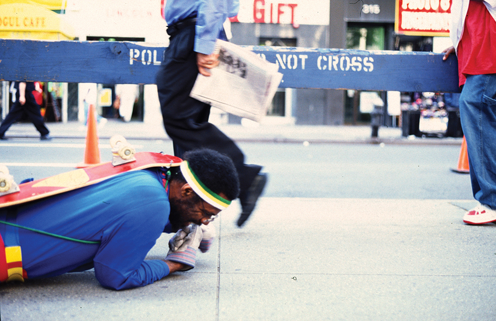 Black man dressed as Superman fallen to the ground in front of police barrier