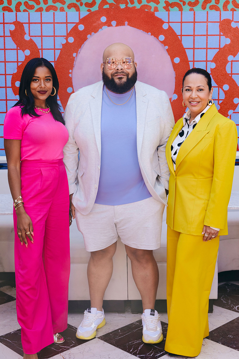 Megan Pinckney Rutherford, Sergio Hudson, and Inga Beckham in bright clothing and standing in a colorful set