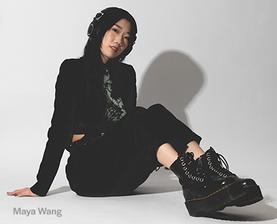 Maya Wang seated on the floor wearing headphones, all black, and creeper boots