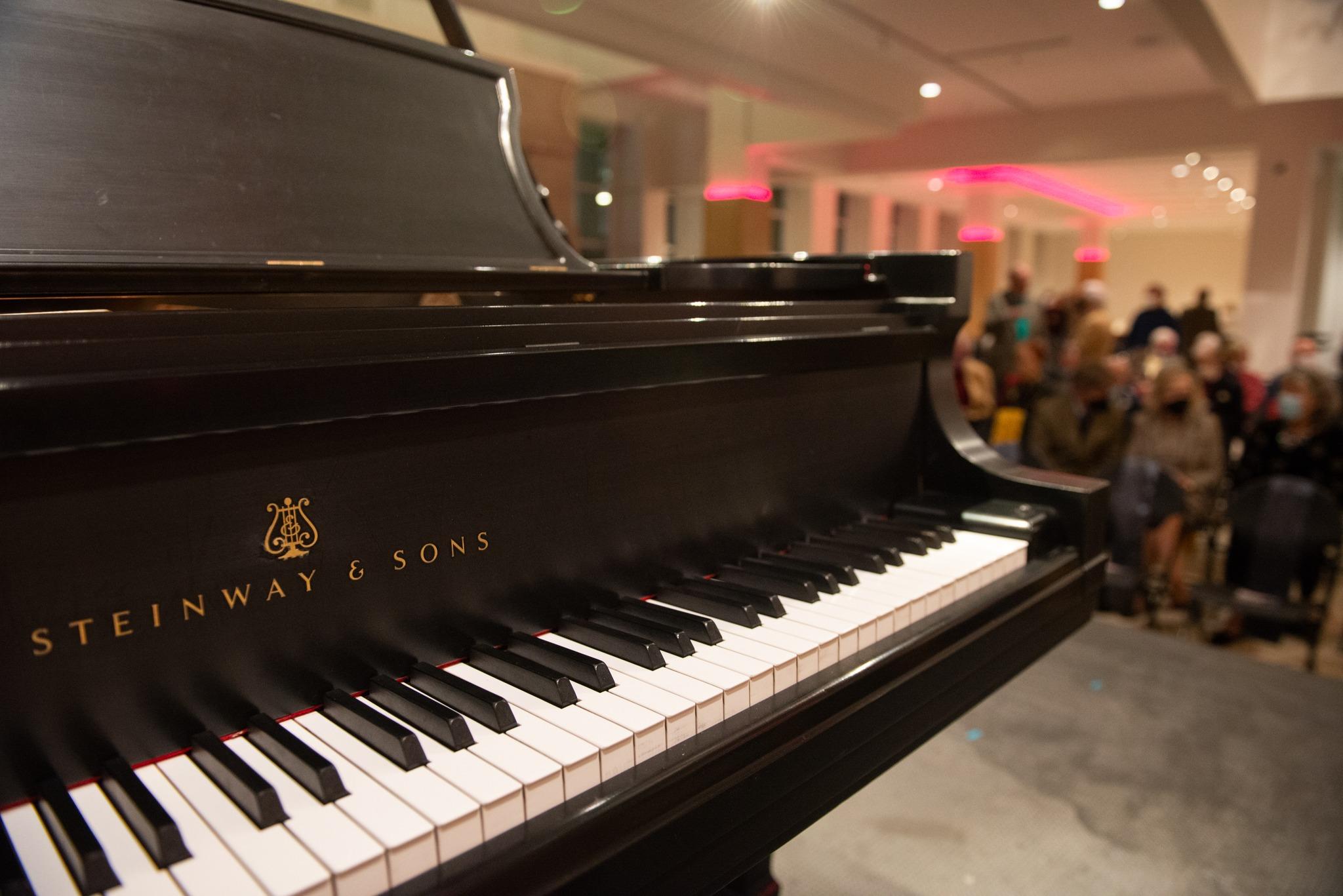 Closeup on the keys of a Steinway & Sons grand piano with an indistinct crowd in the background