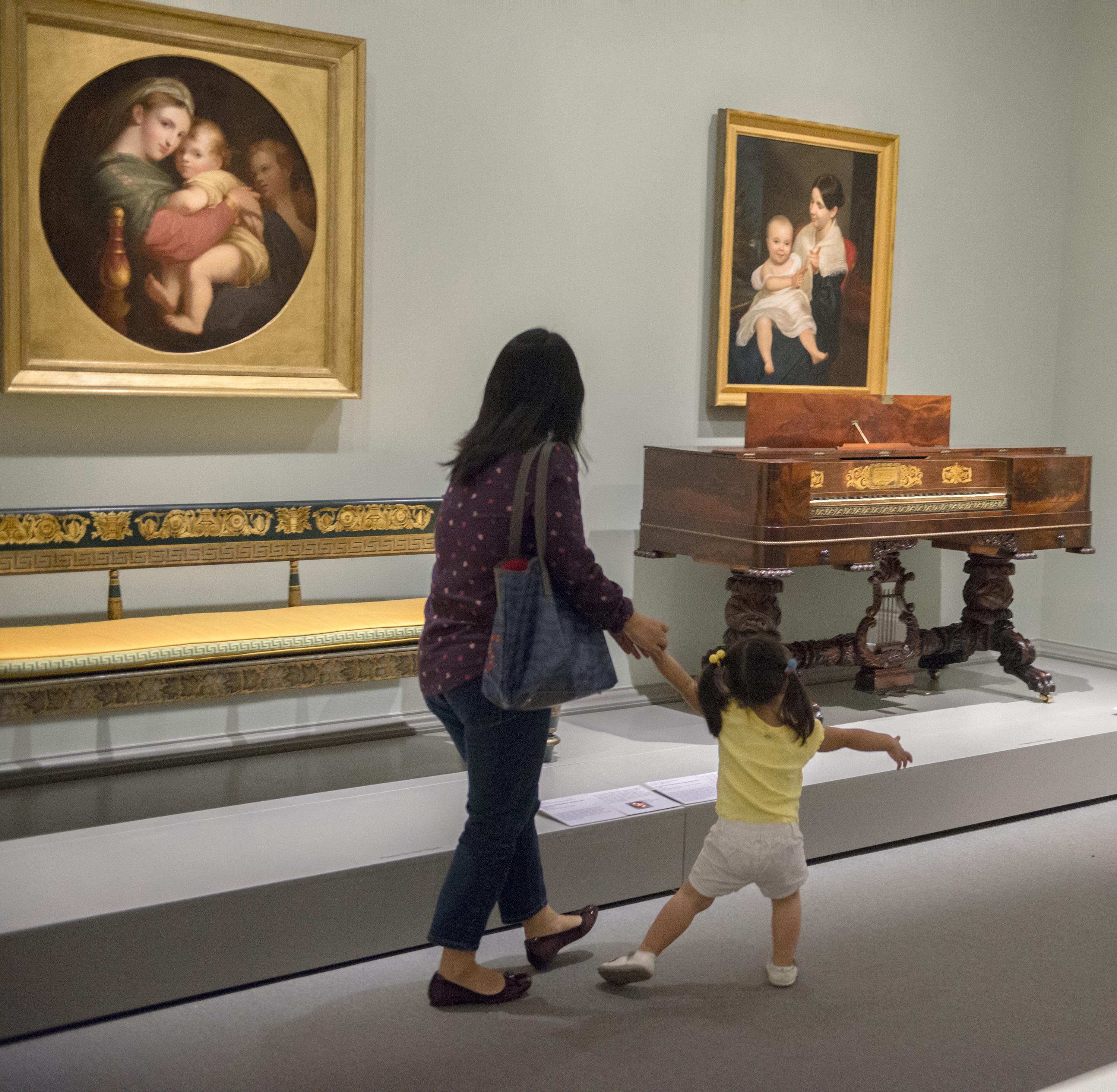 Child and parent moving in gallery with art of people and furniture