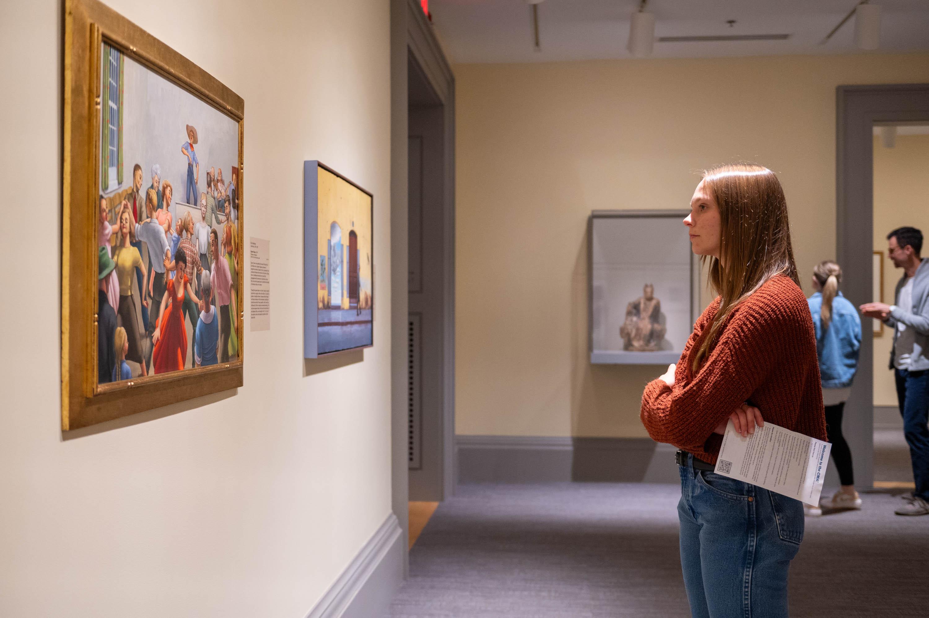 Young white presenting woman looking at Kyra Markham's color painting "Square Dance" in our collection gallery