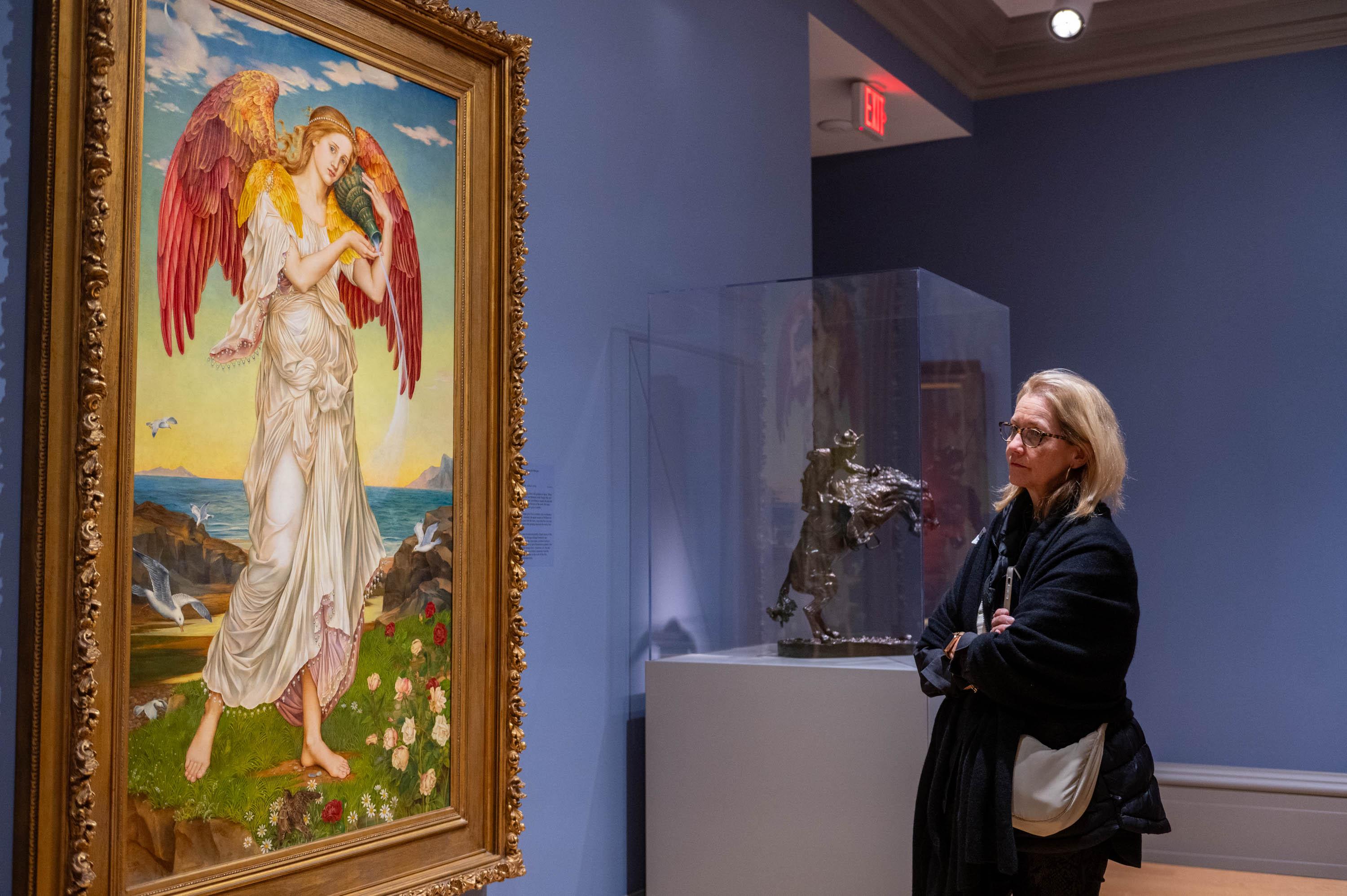 White Woman looking at painting resembling a white angel in white cloth with red wings in a valley type setting