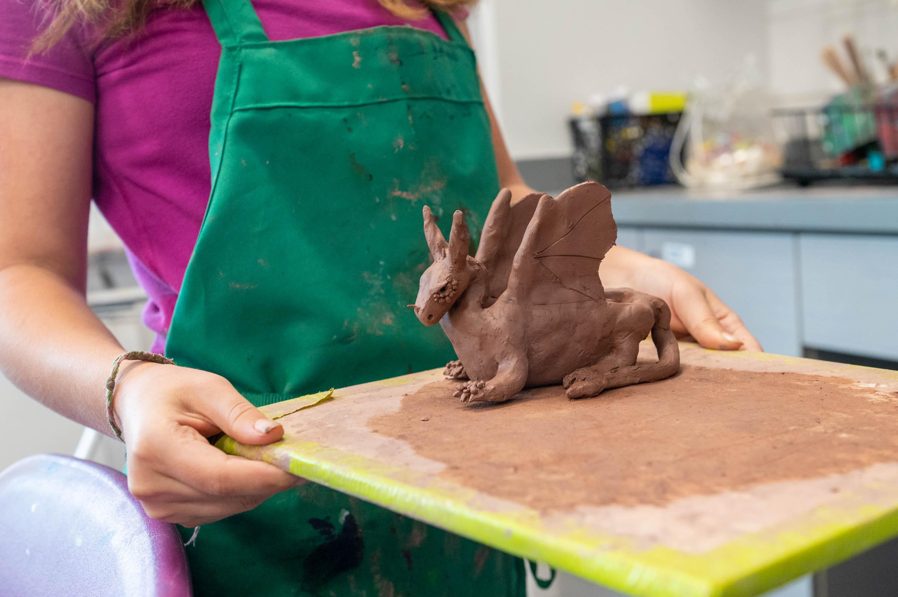 a teen carrying a clay dragon to the kiln
