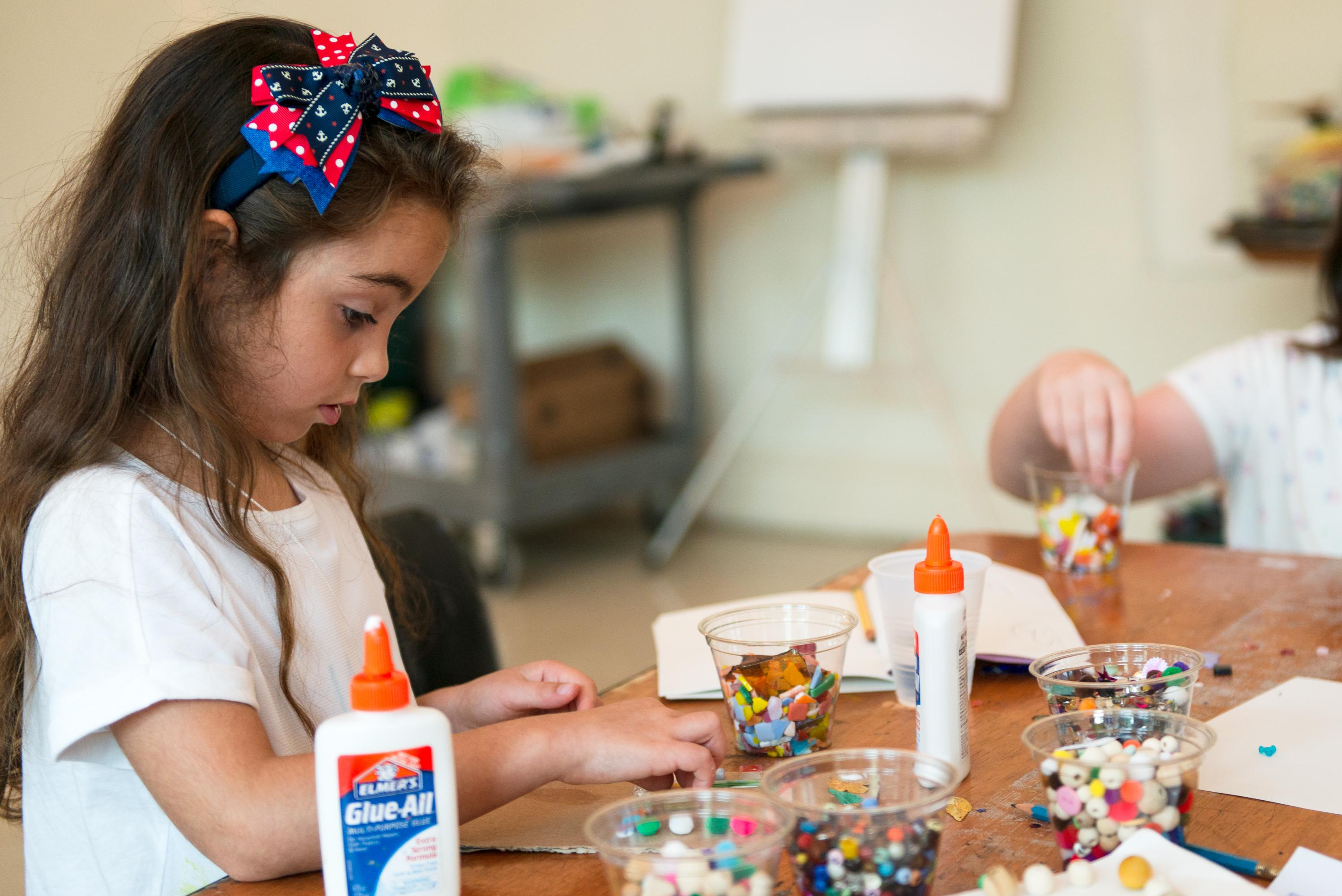 Young child crafting with glue and beads
