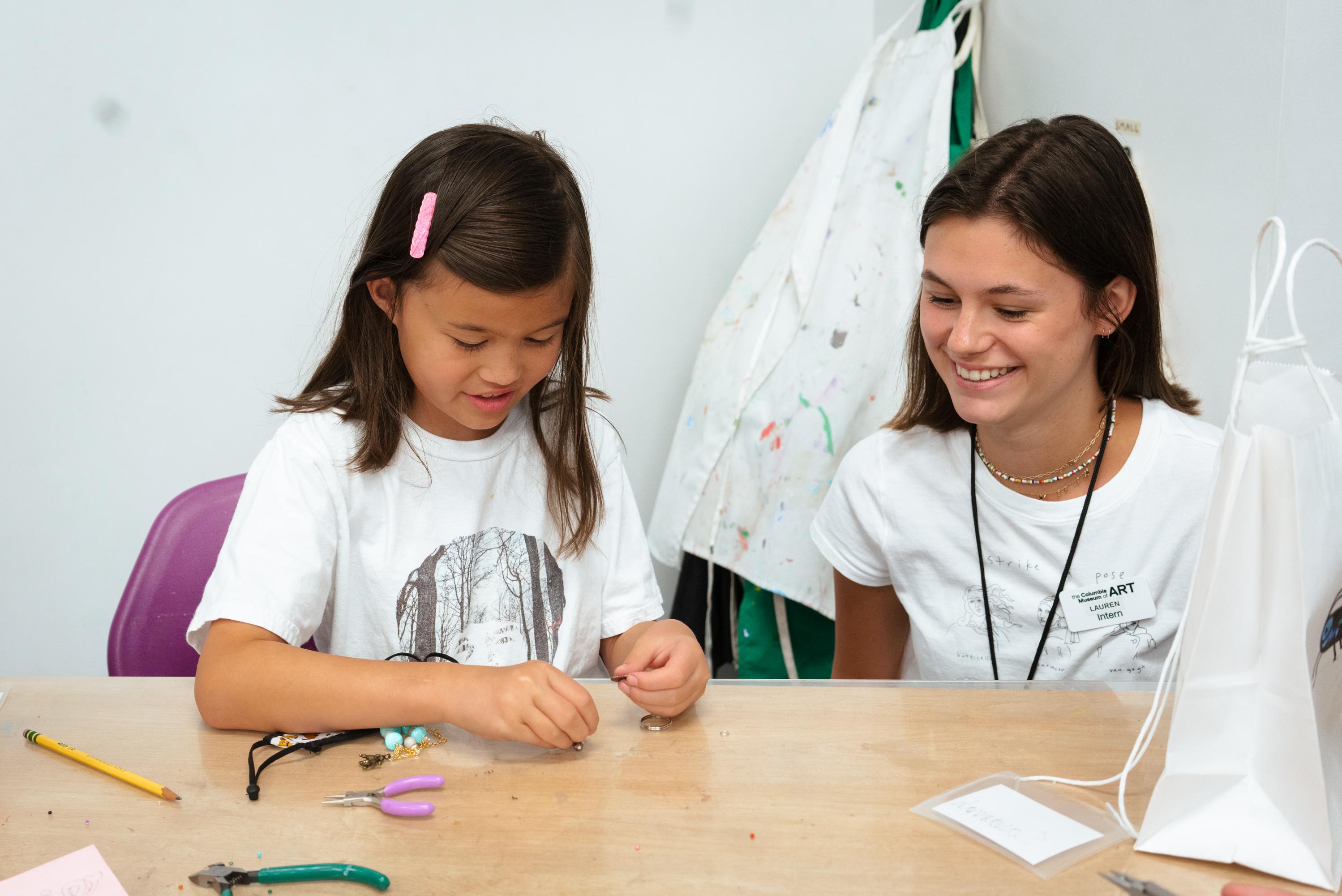 a young girl builds jewelry as an instructor encourages her